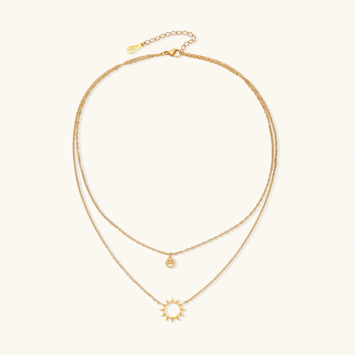 Gold layered necklace set with sunburst and smiley face pendants on delicate chains against white background.